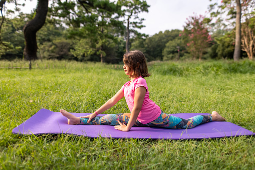 Flexible little girl stretching on yoga mat in public park