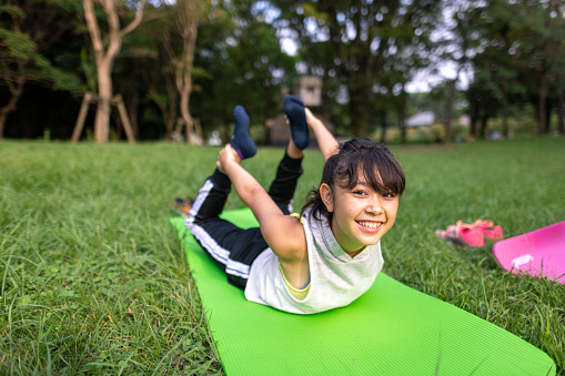 Teenage girl doing yoga on yoga mat in public park - bow pose