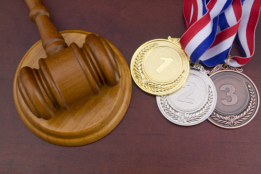 Gold, silver and bronze medals and wooden judge gavel, on table, sport arbitration court concept.