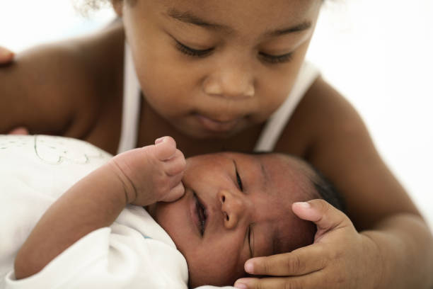 afrikaanse amerikaanse baby die op bed ligt terwijl de zuster het letten op - broer en zus stockfoto's en -beelden
