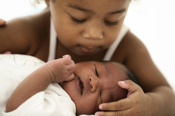 african american infant baby lying on bed while sister watching