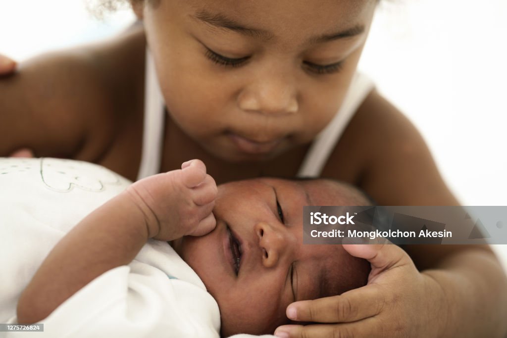 african american infant baby lying on bed while sister watching Baby - Human Age Stock Photo
