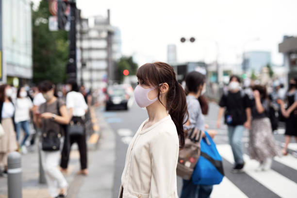 붐비는 거리를 가로 질러 걷는 마스크를 가진 여성 - japan tokyo prefecture city women 뉴스 사진 이미지