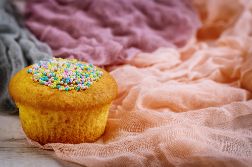 One cupcake with color sprinkles on fabric. Close up.