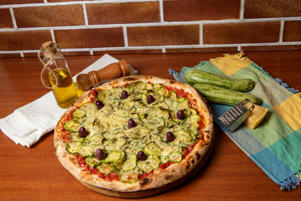 vegetarian pizza of zucchini Delicious italian vegetarian pizza, with tomatoes sauce, peppers, olives and zucchini on wooden table background.  text in portuguese: serenity spicery stock pictures, royalty-free photos & images