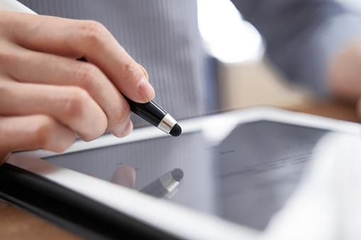 A Japanese businesswoman in her hands signing her digital signature on a tablet while wearing plain clothes