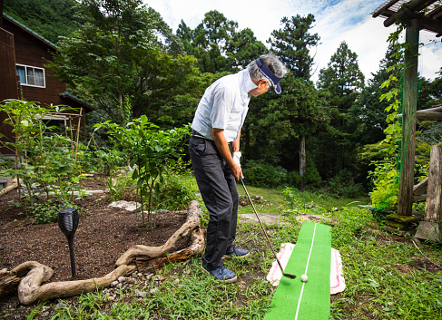 A Japanese senior gentleman practicing Golf at home in the front yard.