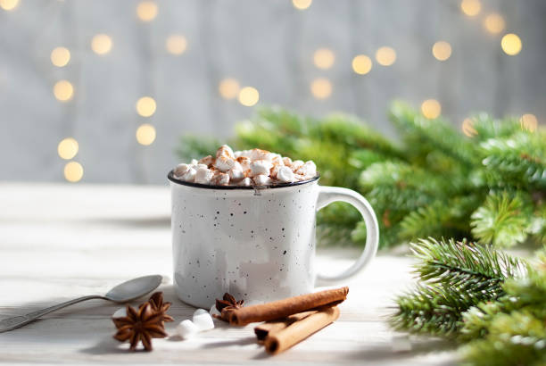 istock Christmas white cup with hot chocolate and marshmallows on with cinnamon sticks with beautiful garland lights 1275770177