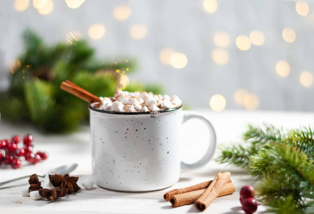 istock Christmas white cup with hot chocolate and marshmallows and red berries on with cinnamon sticks with garland lights 1275770178