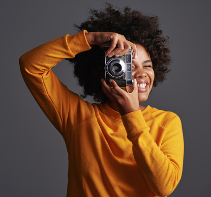 Shot of a young woman taking pictures on a vintage camera against a grey background