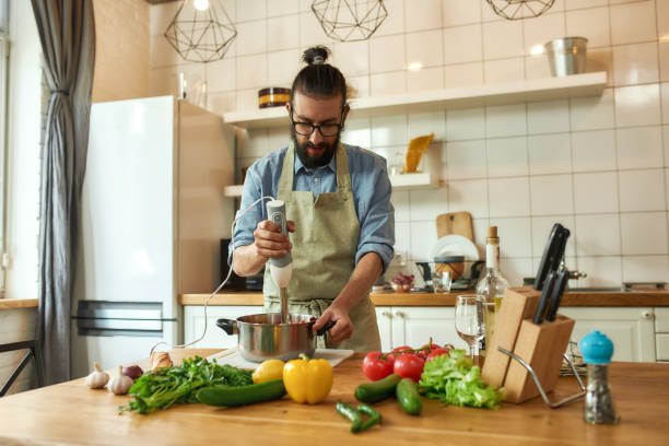 istock Young man, chef cook using hand blender while preparing Italian meal in the kitchen 1275773163