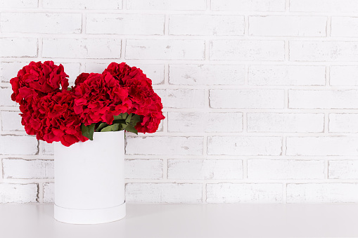 red flowers in vase in the table over white brick wall