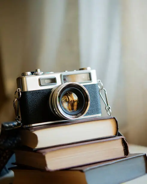 Three vintage books and a film camera are stacked on the table indoors. Books lie on a blurred background.