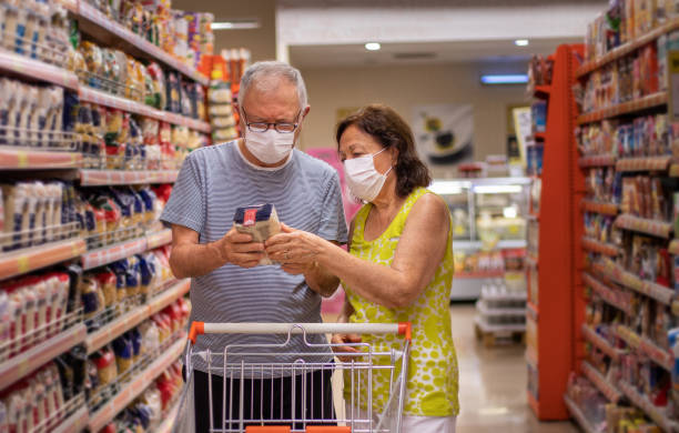 un couple de personnes âgées faisant du shopping au marché avec des masques de protection. - high calorie photos et images de collection