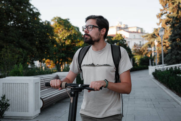 istock Attractive man riding a kick scooter at cityscape background 1275789135