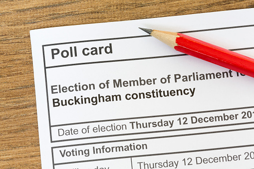 Poll card for a UK general election, voting information paper on desk with pencil