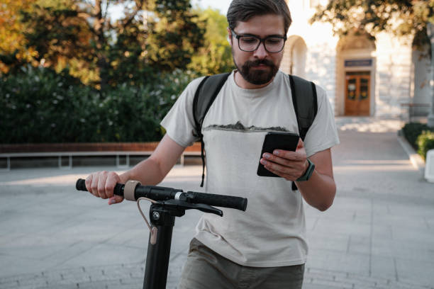 istock hipster man commuter with electric scooter outdoors in city, using smartphone 1275792283