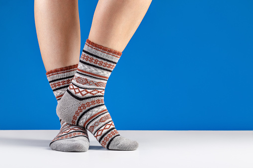 Women's feet have warm knitted socks with an ornament. Blue background, studio shot.