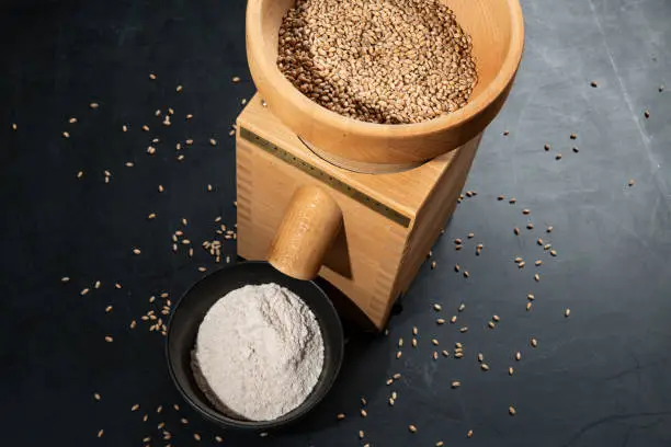 Grain mill on a black plate with spelt and flour