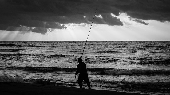 Overcast cloudy weather. Sunrise is the earliest hours of the morning. Silhouette fisherman fishing on the beach