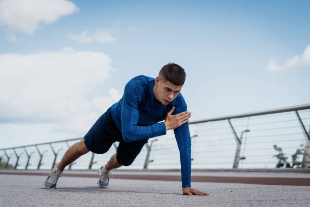 Young adult sportsman making sport training outdoors alone Concept of workout and exercise. Low angle view of young adult sportsman doing shoulder tap exercise, push up and standing in plank pose, making sport training outdoors alone bodyweight training stock pictures, royalty-free photos & images