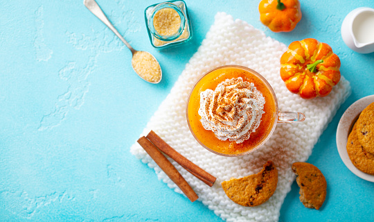 Pumpkin spice latte in glass cup with cookies. Blue background. Copy space. Top view.