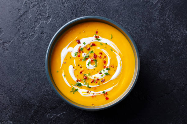 istock Butternut squash soup with cream in black bowl. Dark background. Top view. 1275801536