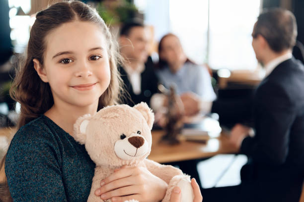Beautiful girl with parents stands in the office. A young girl stands with a teddy bear and smiling at camera. Beautiful girl with parents stands in the office of a lawyer. adoption stock pictures, royalty-free photos & images