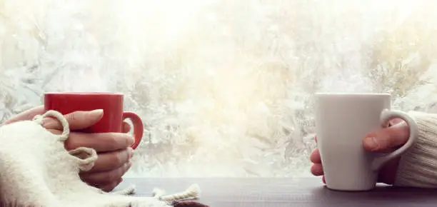 red and white mugs in hands against the background of a frosty window