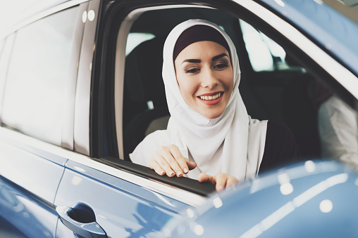 Arab woman sits in a new car and looks out of the window. A woman sits in a new car and wants to buy it at a car dealership.