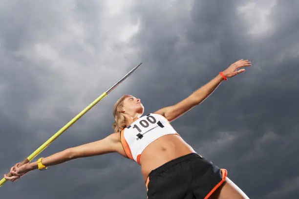 Female athlete throwing javelin against cloudy sky low angle view