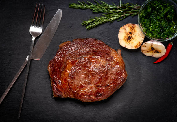 rindfleisch gegrillt rib auge steak auf schwarzem stein teller mit gewürzen, gabel und messer, fleisch-diät, top-ansicht - chimichurri horizontal beef steak stock-fotos und bilder