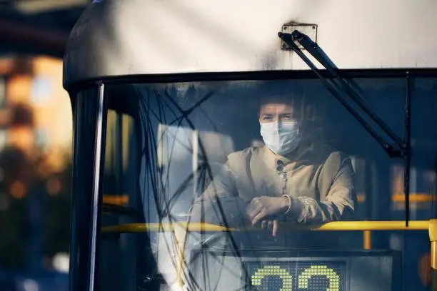 Man wearing face mask and looking from window of tram. Themes public transportation in new normal, coronavirus and personal protection.