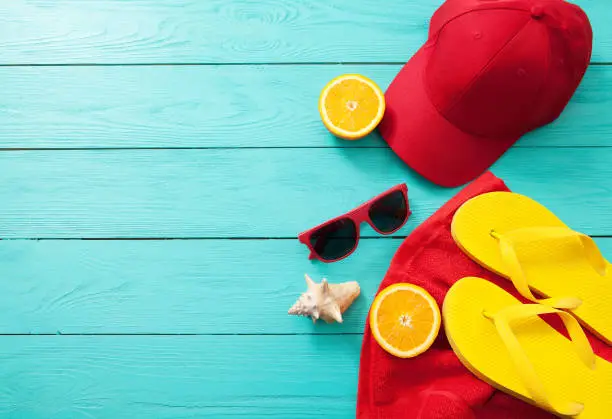 Photo of Summer accessories. Flip flops, sunglasses, towel, red cap and oranges on blue wooden background. copy space.