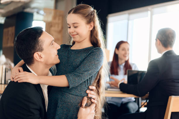 Adult father hugs little daughter. Adult father hugs little daughter, standing in foreground. Young parents argue about one who will take guardianship of little daughter in lawyers office. legislator photos stock pictures, royalty-free photos & images