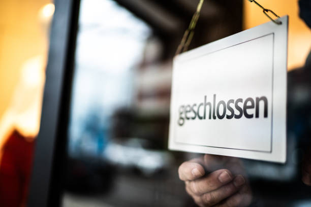 Business ower holding closed sign (geschlossen) on storefront door Business ower holding closed sign (geschlossen) on storefront door german language photos stock pictures, royalty-free photos & images