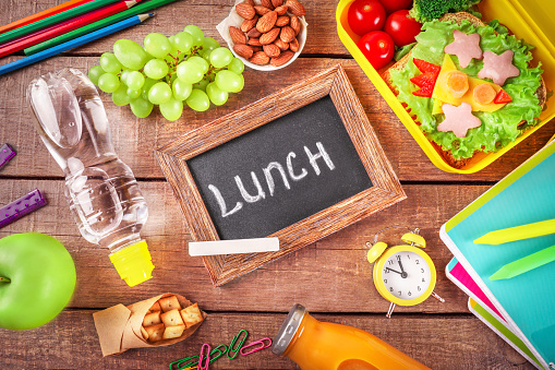 Lunch time. Healthy school lunch box and school stationery on wooden background. Top view.