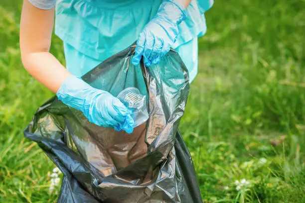 Child collects plastic trash from grass throwing garbage in garbage bag in the park