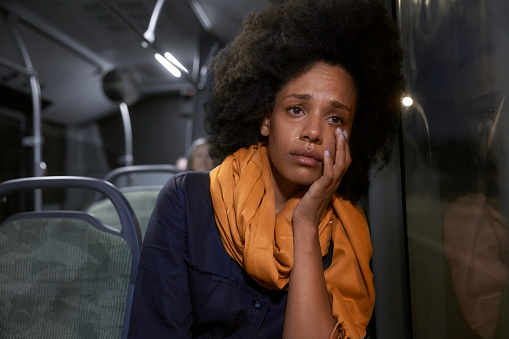 Sad african-american young woman with afro hair sitting on public bus crying wiping tears