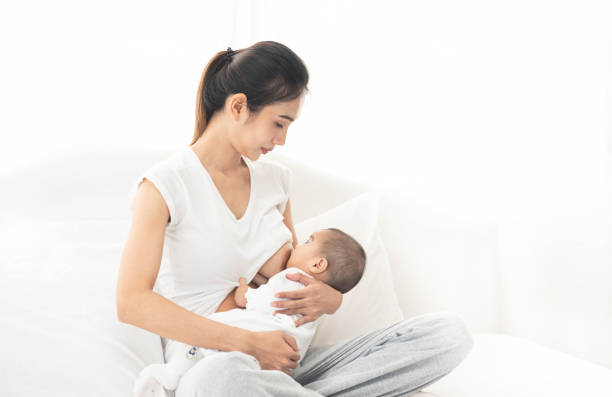 giovane madre asiatica che allatta il seno il suo bambino a casa male in camera bianca - sucking asian ethnicity baby mother foto e immagini stock