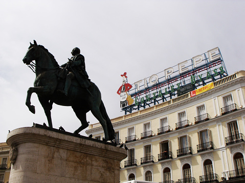 Madrid, Spain, August 15, 2015: Monument to King Carlos III and the typical Tio Pepe poster in Puerta del Sol square. Madrid