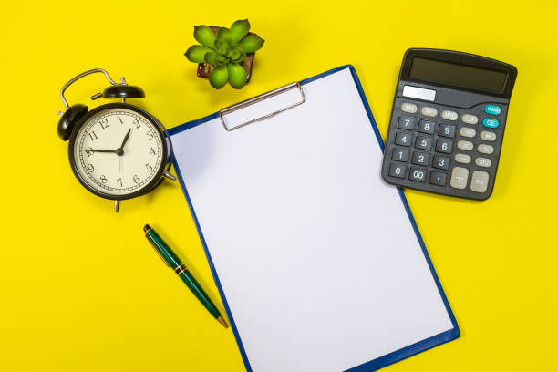 istock Stationery or essential office tools. Workplace pen with sheets of office paper, calculator, flower and alarm clock on yellow background, top view. 1275835942