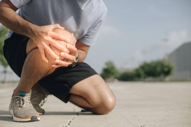 Young Asian man suffering from knee pain outdoor, Injury from workout concept stock photo