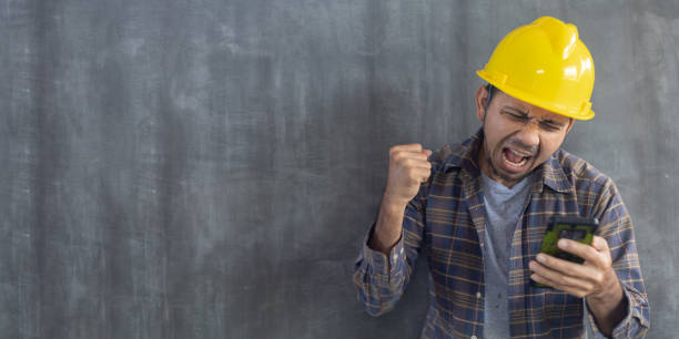 istock Construction man looks at the smartphone screen and rejoices hands up on cement wall background with copy space 1275838142