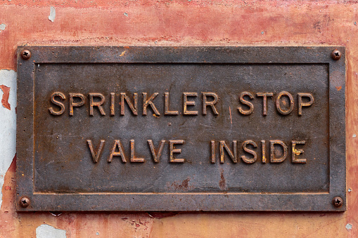 Old metal sign showing the location of a sprinkler stop valve.