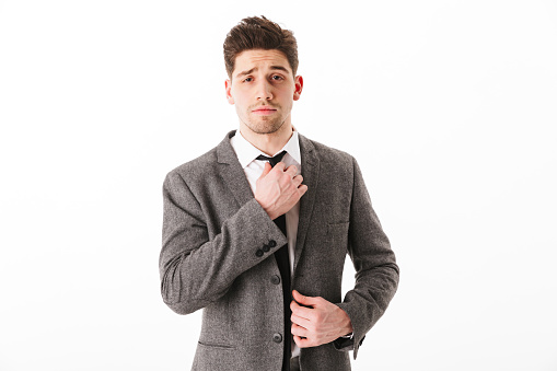 Concentrated business man in jacket corrects his tie and looking at the camera over white background