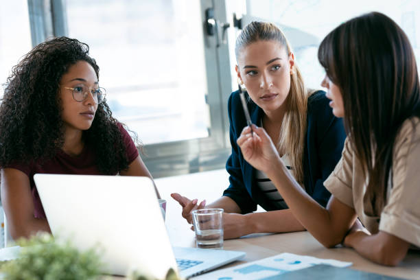 istock Three modern businesswomen talking and reviewing the latest work done on the computer in a joint workspace 1275841023
