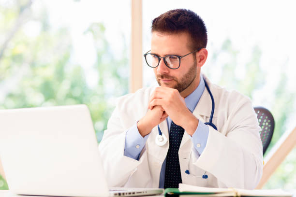 istock Male doctor sitting at desk and using laptop while working in doctor's office 1275841145