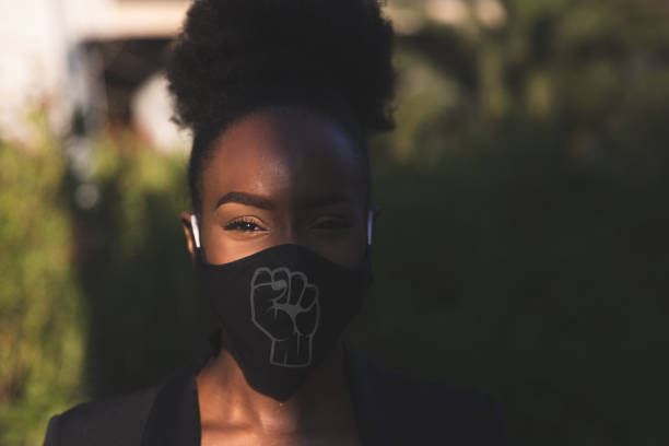 Woman wearing a black face mask with a fist printed on it Woman wearing a black face mask with a fist printed on it, protesting for human rights of black people. anti racism photos stock pictures, royalty-free photos & images