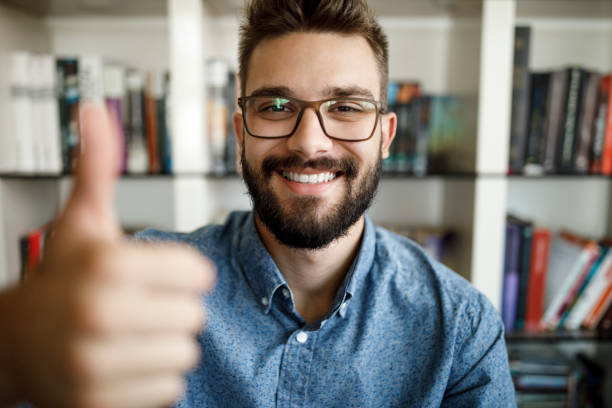 point de vue de la caméra du jeune homme retenant des pouces vers le haut au bureau à la maison - video conference camera photos et images de collection